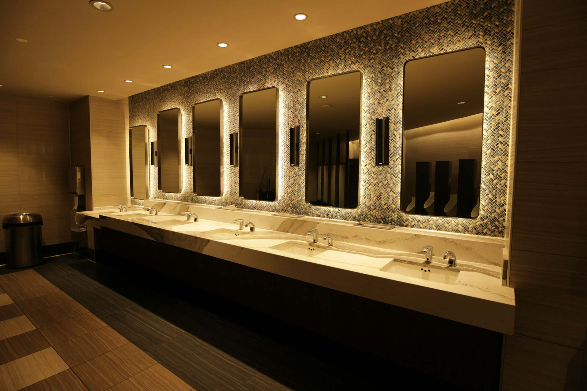 Commercial public restroom vanity units with multiple basins and illuminated mirrors